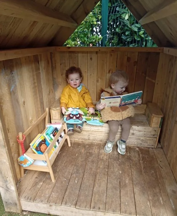 A child reading in a wooden play hut at Roobyloos Nursery